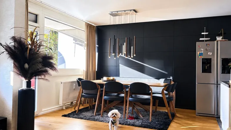 Moderner Essbereich mit Holzboden, großem Esstisch und dunkler Akzentwand, beleuchtet von einer stilvollen Hängelampe.