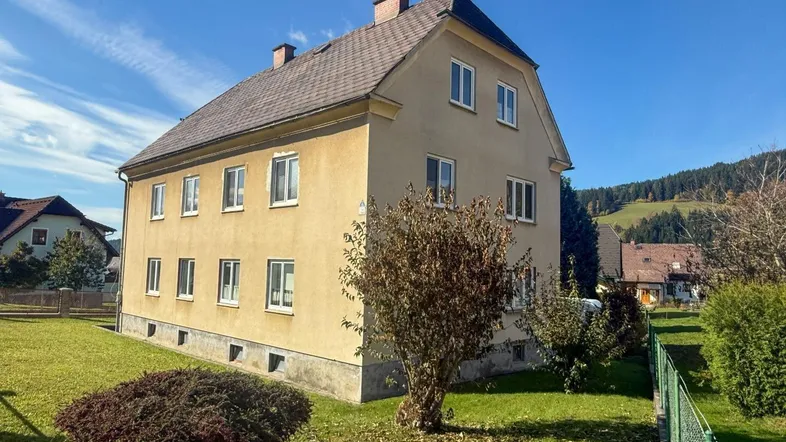 Freistehendes Haus mit gelber Fassade und Satteldach, umgeben von Grünflächen.