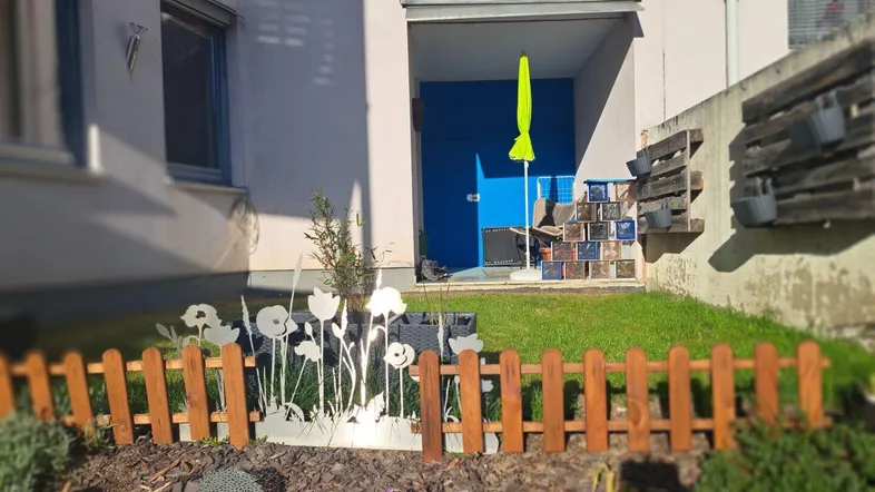 Kleiner, sonniger Gartenbereich mit Zaun und Blick auf den Hauseingang.
