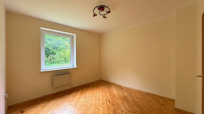 Helles Zimmer mit Holzboden und Fenster, das viel natürliches Licht hereinlässt.
