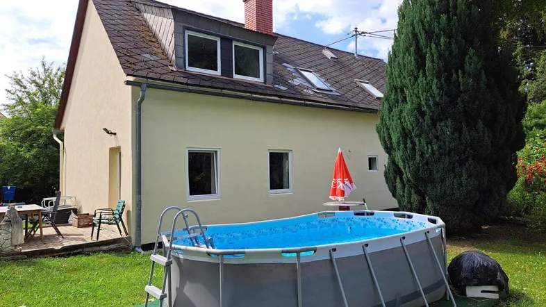 Gartenbereich mit oberirdischem Pool, Rasenfläche und einer kleinen Terrasse am Haus.