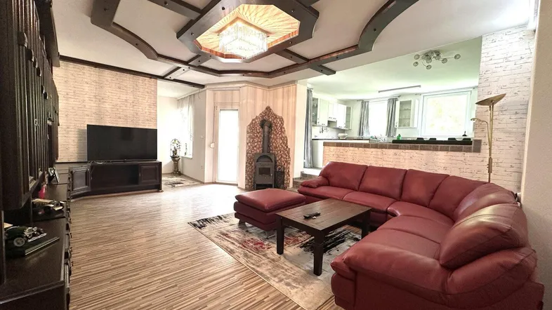 Geräumiges Wohnzimmer mit Holzbalkendecke, Kaminofen und offener Verbindung zur Küche.