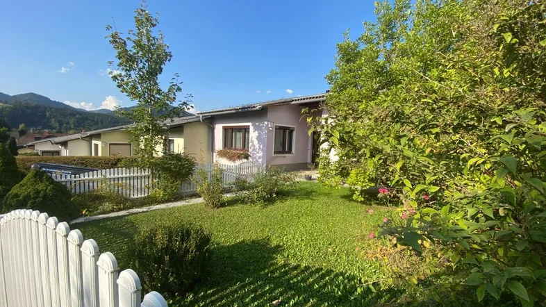 Gepflegter Vorgarten mit Rasenfläche und weißem Zaun vor dem Einfamilienhaus unter blauem Himmel.