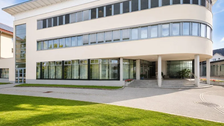 Modernes Bürogebäude mit geschwungener Fassade, großen Fenstern und gepflegter Grünfläche.