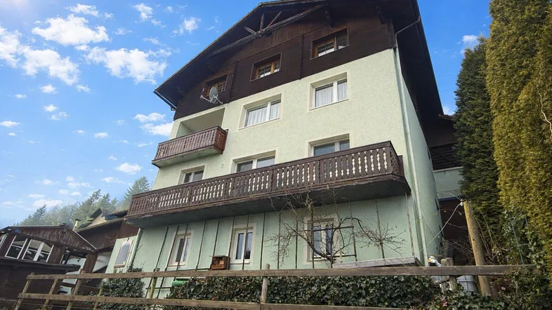 Traditionelles Wohnhaus mit mehreren Balkonen und grüner Umgebung unter blauem Himmel.