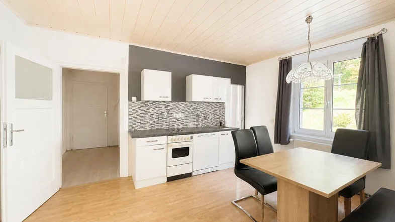 Helle Küche mit weißer Einbauküche, Essbereich und Holzdecke.