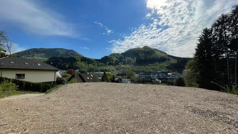 Weitläufiges Grundstück mit Schotterfläche und Blick auf die umliegende Berglandschaft unter blauem Himmel.