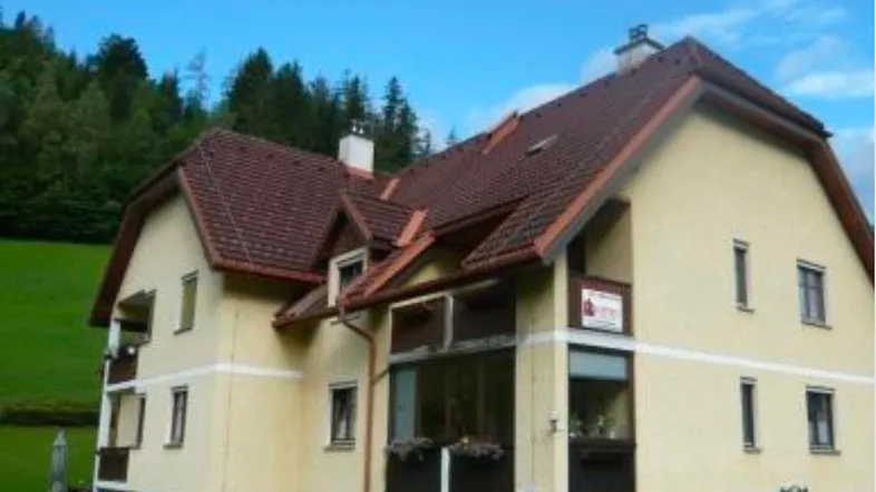 Traditionelles Haus mit Satteldach und Balkonen, umgeben von grüner Landschaft und Bäumen.