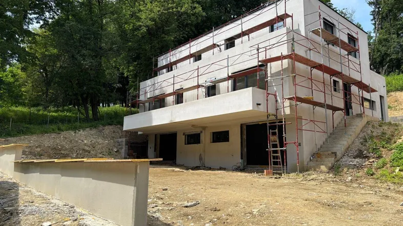 Neubau im Rohbauzustand mit Gerüst, umgeben von viel Grün und Baustelle.