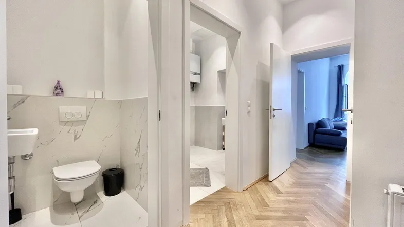 Heller Flur mit Fischgrätparkett und Zugang zu einem modernen Gäste-WC mit Marmoroptik-Fliesen.