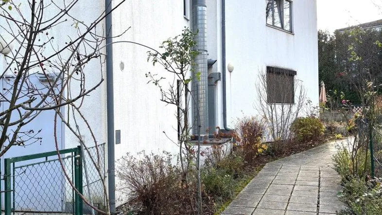 Seitenansicht eines Wohnhauses mit gepflastertem Weg und Gartenbereich bei sonnigem Wetter.