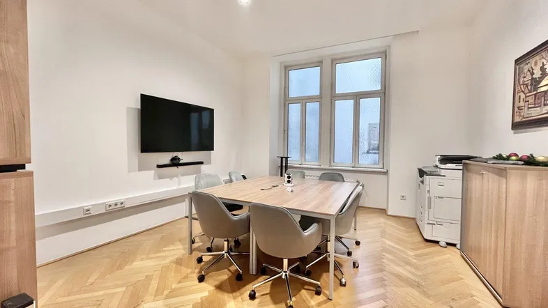 Heller Konferenzraum mit modernem Holztisch, ergonomischen Stühlen und großem Bildschirm für Präsentationen.