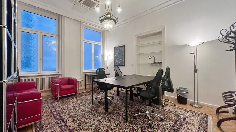 Geräumiges Büro mit Konferenztisch, bequemen roten Sesseln und einem gemusterten Teppich.