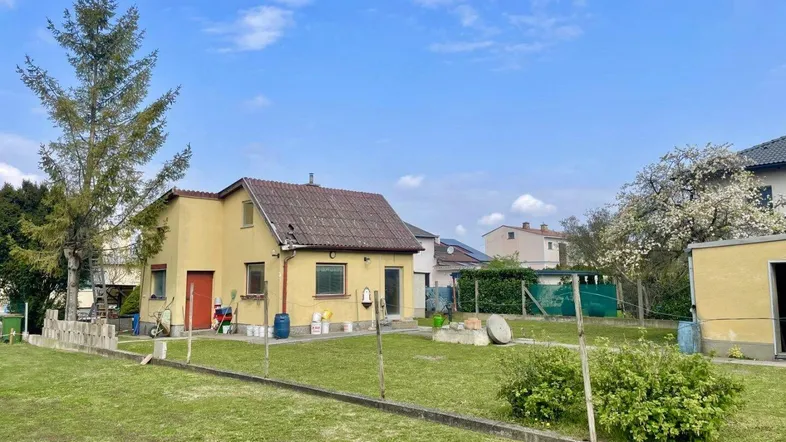 Kleines gelbes Haus mit Satteldach und großem Gartenbereich, umgeben von Grün.