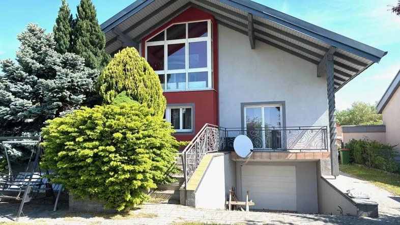 Modernes Einfamilienhaus mit roter Akzentfassade, großem Fenster und Balkon.