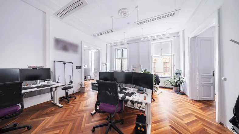 Großes, offenes Büro mit mehreren Arbeitsplätzen, Fischgrätparkett und hohen Fenstern.
