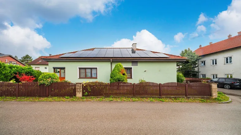 Einfamilienhaus mit hellgrüner Fassade, Photovoltaikanlage auf dem Dach und Holzzaun.