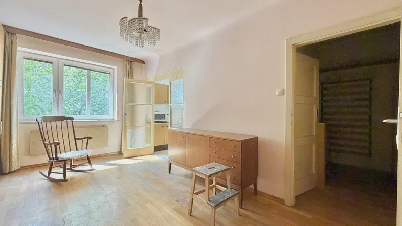 Helles Wohnzimmer mit Holzparkett, großem Fenster und Blick ins Grüne, ausgestattet mit einem Kronleuchter.