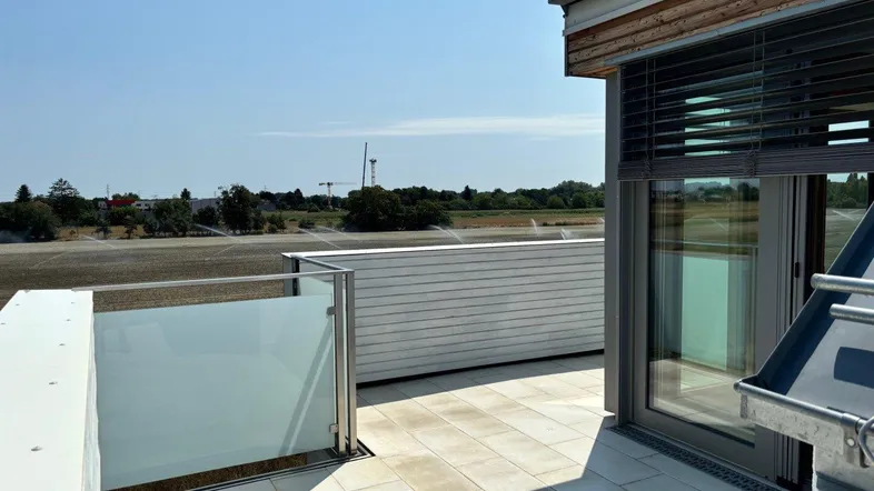 Helle Dachterrasse mit Fliesenboden, Glasgeländer und weitem Blick über die Landschaft.