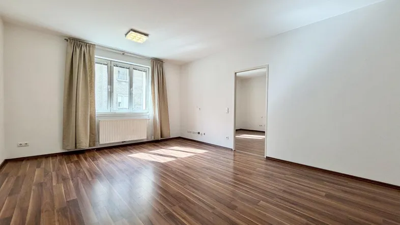 Helles Zimmer mit Laminatboden und Fenster mit Vorhängen, bereit zur Einrichtung.