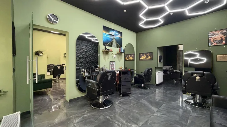 Moderner Friseursalon mit stilvoller Einrichtung, dunklen Fliesen und auffälliger Wabenbeleuchtung an der Decke.