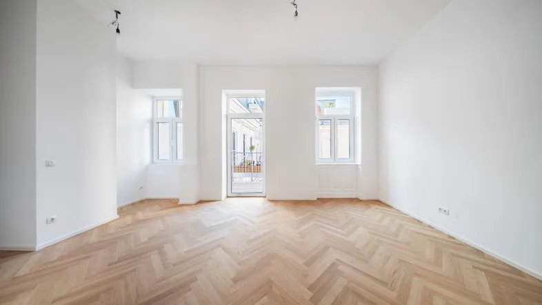 Helles Zimmer mit Fischgrätparkett und Zugang zu einem kleinen Balkon, ideal für Wohnzwecke.