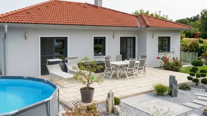 Modernes Einfamilienhaus mit großer gepflasterter Terrasse, Garten und einem Aufstellpool im Außenbereich.