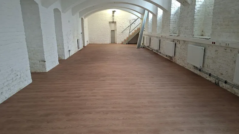 Großer, leerer Raum mit Holzboden, weiß gestrichenen Ziegelwänden und gewölbten Decken.