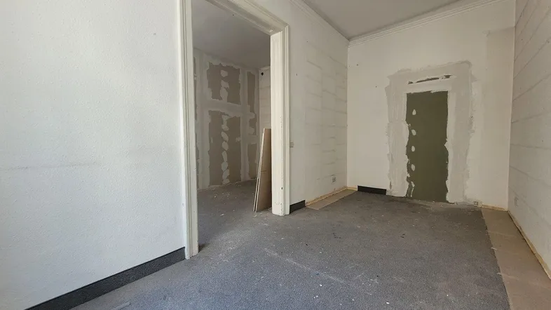 Unfertiger Innenraum mit verputzten Wänden und altem Teppichboden, bereit für die Renovierung.