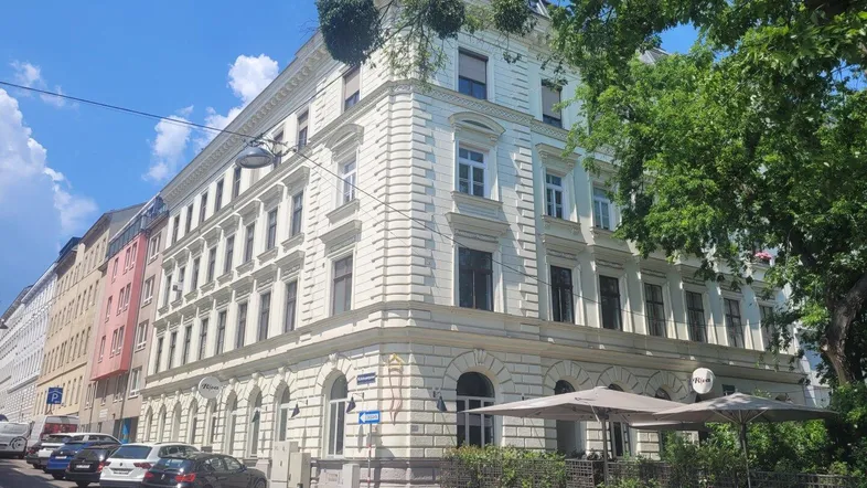 Klassisches Wiener Wohngebäude mit historischer Fassade und Straßencafé im Erdgeschoss.