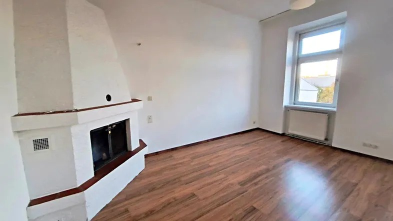 Helles Zimmer mit Kamin und Holzfußboden, ideal als Wohn- oder Schlafzimmer nutzbar.