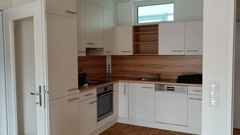 Moderne Einbauküche mit weißen Schränken, Holzakzenten, integrierten Geräten und Parkettboden.