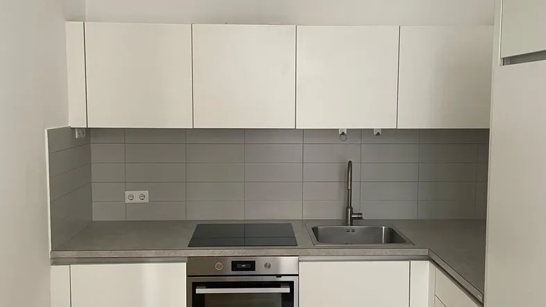 Moderne Einbauküche mit weißen Schränken, Induktionskochfeld und Backofen, ergänzt durch Fischgrätparkett.
