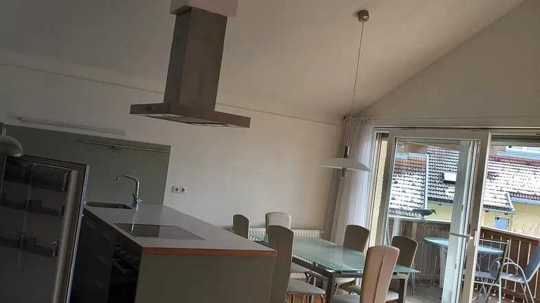 Offener Wohn- und Essbereich mit integrierter Küche, Holzbalken und Zugang zu einem Balkon.