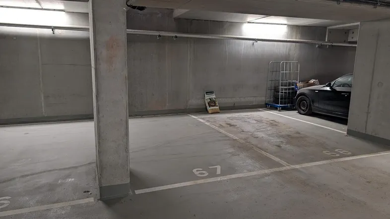 Geräumige Tiefgarage mit markierten Stellplätzen und sichtbaren Installationen an der Decke.