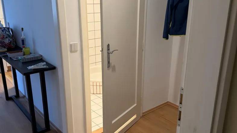 Heller Flur mit Holzboden und Zugang zu einem Badezimmer, das eine Dusche zeigt.