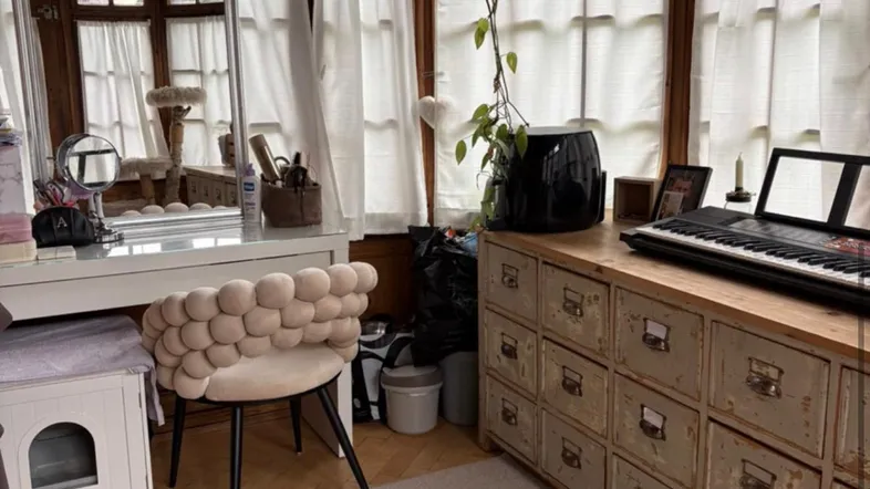 Helles Zimmer mit vielen Fenstern, Holztäfelung, Schminktisch und einem langen Schrank mit Tastatur.