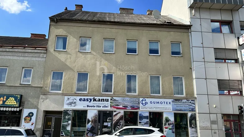 Mehrstöckiges Gebäude mit Geschäftsflächen im Erdgeschoss und Wohnungen darüber an einer städtischen Straße.