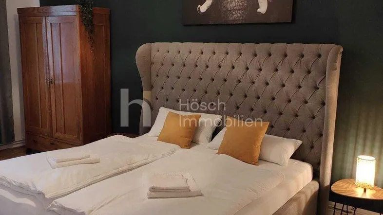 Gemütliches Schlafzimmer mit großem gepolstertem Bett, dunkler Akzentwand und Parkettboden.