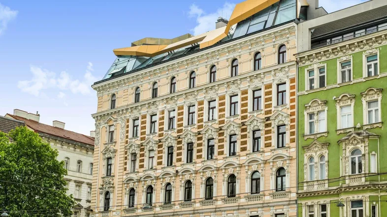 Ornate Fassade eines historischen Gebäudes mit moderner Dachaufstockung unter blauem Himmel.