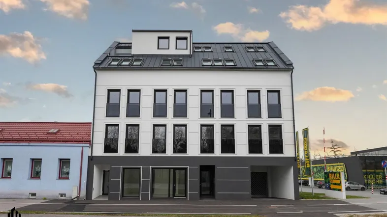 Modernes Gebäude mit weißer und grauer Fassade, großen Fenstern und Satteldach.