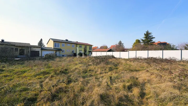 Weitläufiges Grundstück mit Grasfläche und Häusern im Hintergrund unter blauem Himmel.