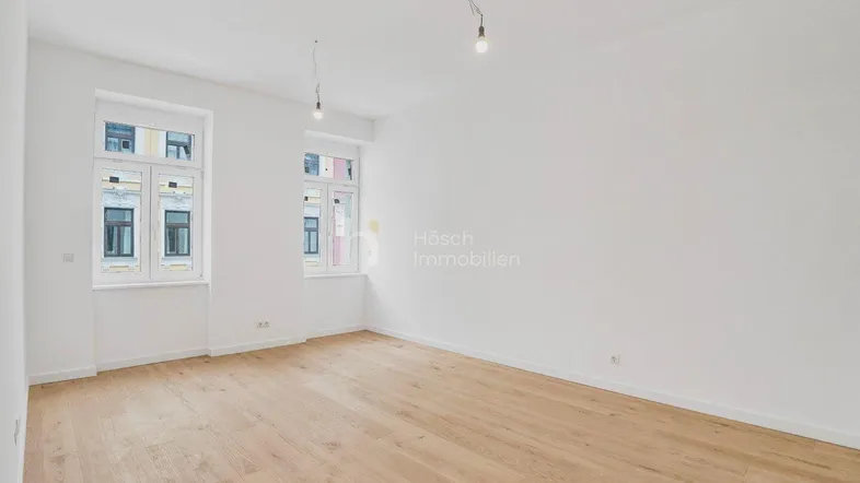 Heller, leerer Raum mit Holzboden und zwei Fenstern, bereit zur individuellen Gestaltung.