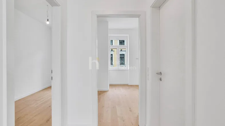 Heller Flur mit Holzboden und Zugang zu verschiedenen Räumen, der einen Blick auf ein Fenster im Hintergrund bietet.
