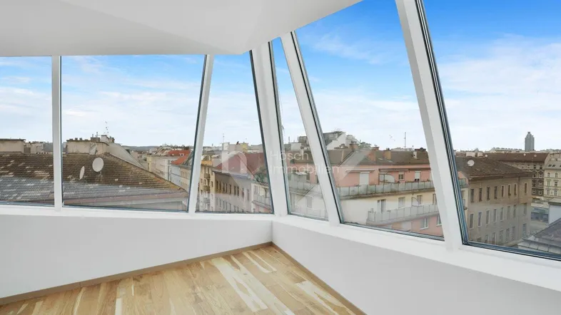 Heller Raum im Dachgeschoss mit großen Schrägfenstern und weitem Stadtblick über die Dächer.