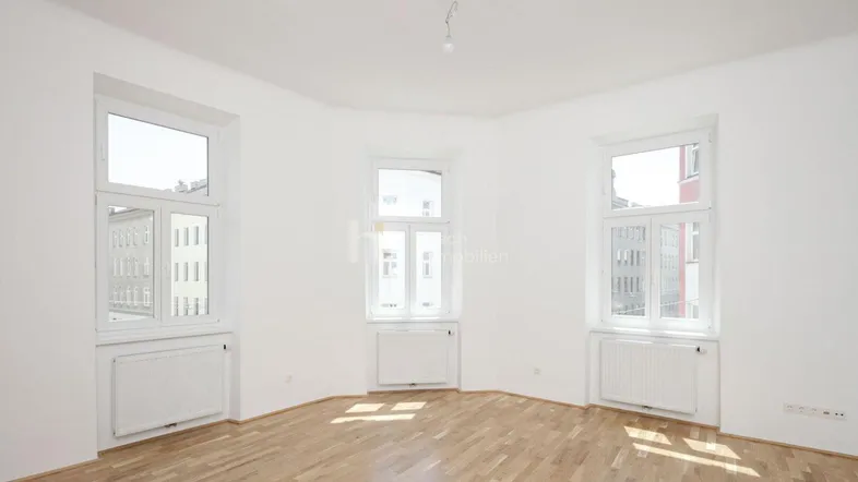Helles Zimmer mit Parkettboden und mehreren Fenstern, ideal als Wohn- oder Schlafbereich.