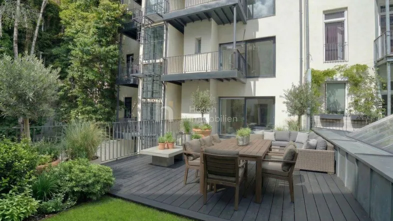 Große Terrasse mit Holzdeck, Gartenmöbeln und Blick auf die moderne Gebäudefassade mit viel Grün.