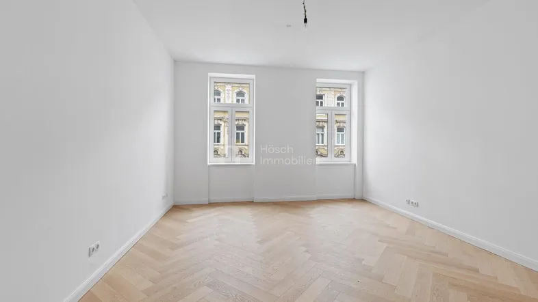 Helles, leeres Zimmer mit Fischgrätparkett und zwei Fenstern, bereit zur individuellen Gestaltung.