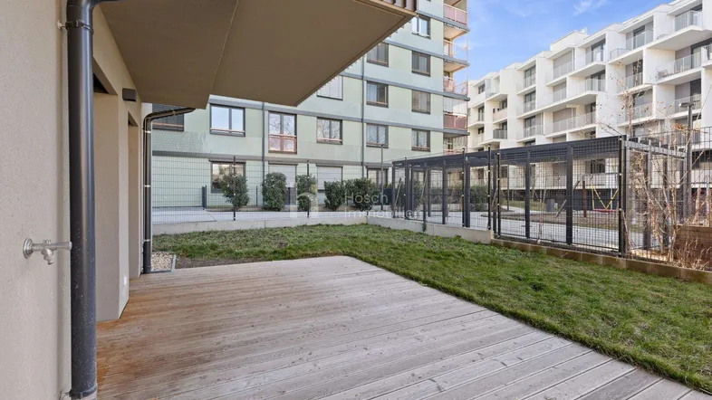 Geräumige Holzterrasse mit angrenzender Rasenfläche und Blick auf moderne Wohngebäude.