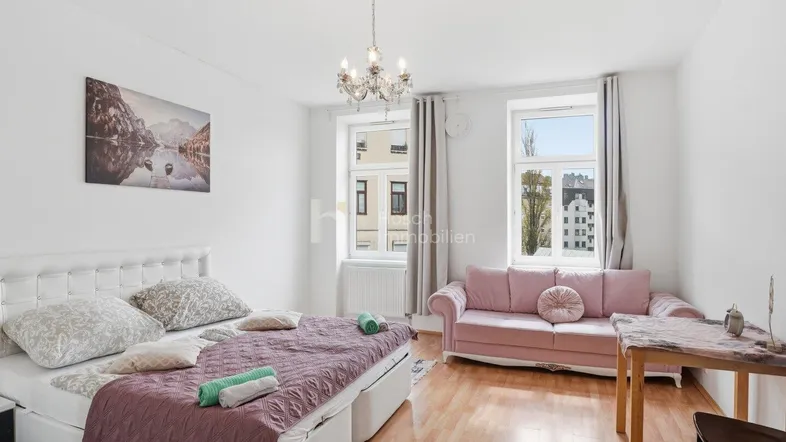 Helles Schlafzimmer mit Doppelbett, rosa Sofa und Holzboden, ideal für eine gemütliche Wohnatmosphäre.